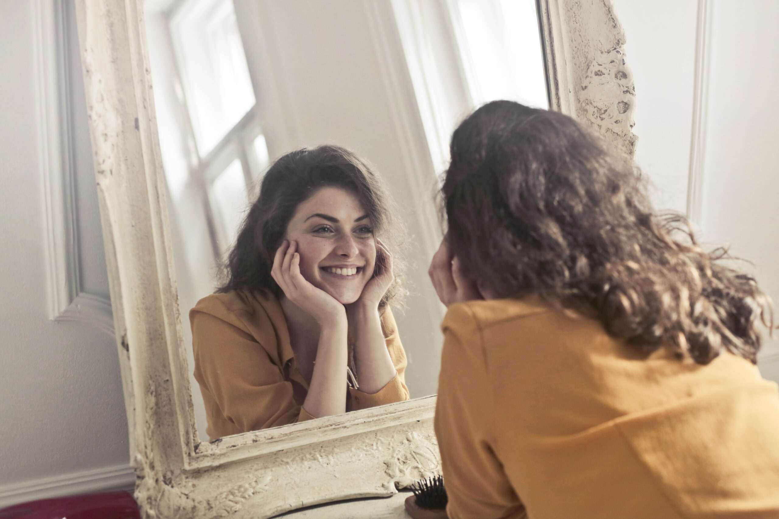 žena se dívá do zrcadlo a usmívá se.