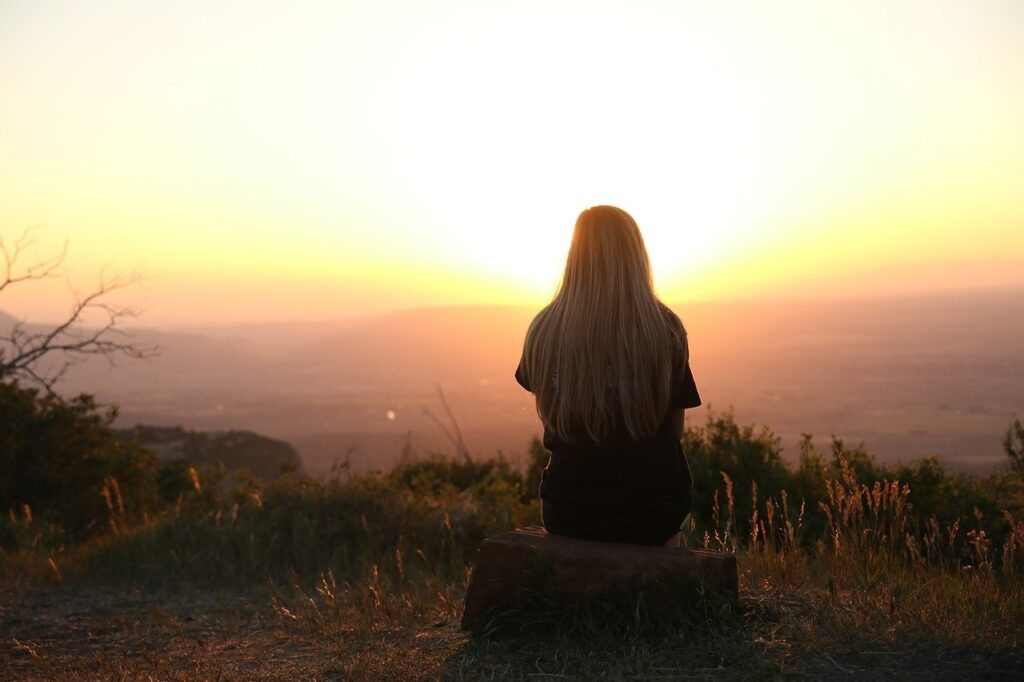 Dívka sedící zády, pozoruje východ slunce.