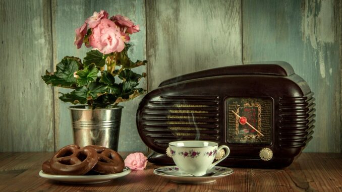 Staré radio, starý porcelánový hrníček s čajem a v pozdí květina.