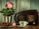 Staré radio, starý porcelánový hrníček s čajem a v pozdí květina.