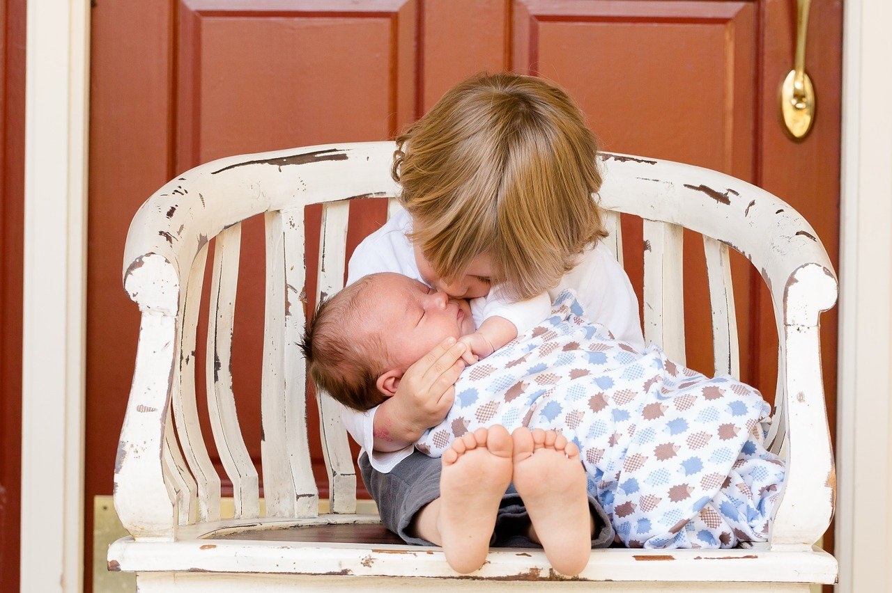 Dvě děti na laviččce, jede z nich je novorozené miminko.