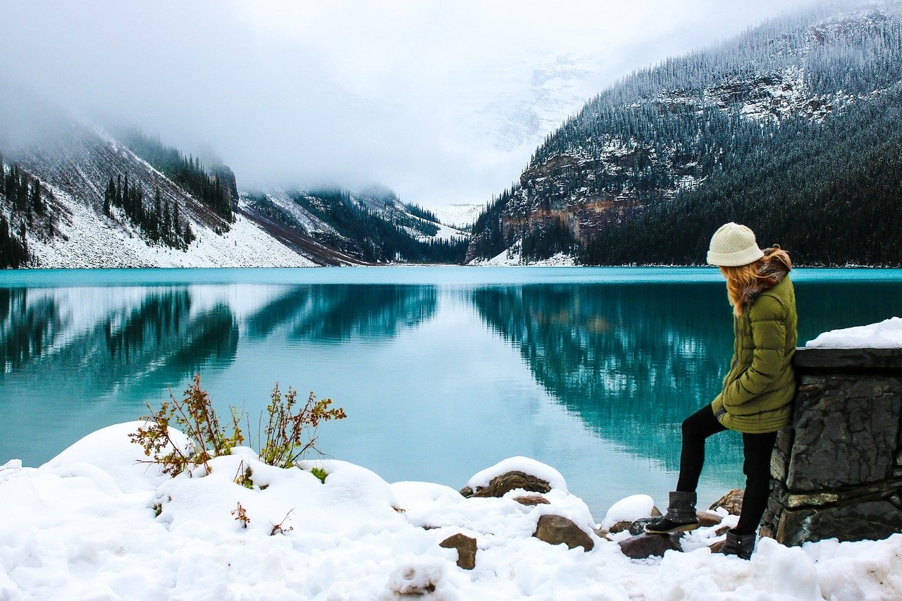 Žena stojí u horského jezera v zimě.