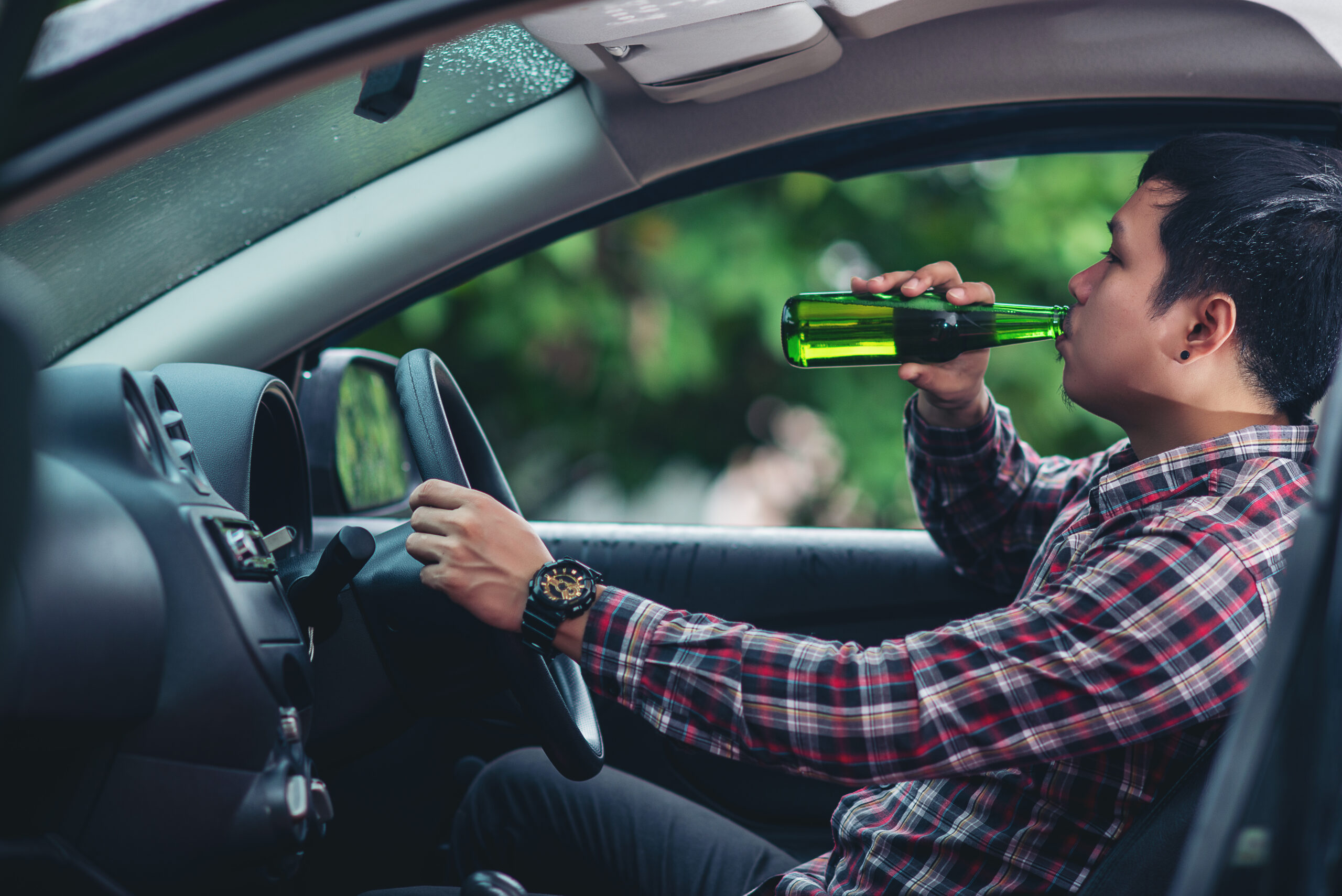 Muž při řízení popíjí pivo z lahve.