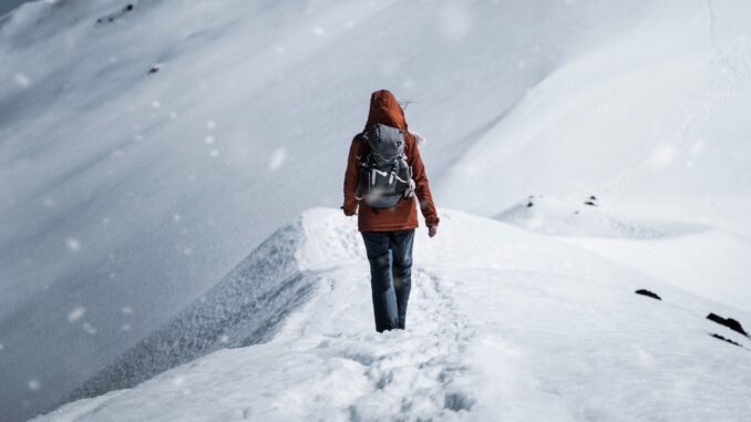 Žena se prochází po hřebeni zasněženého kopce.
