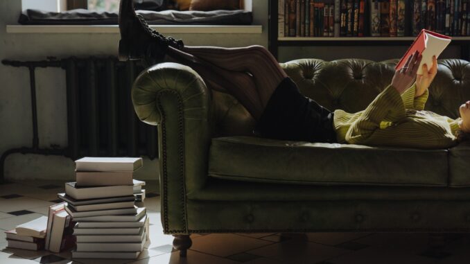 Hromada knih vedle gauče a dívka co na gauči čte.