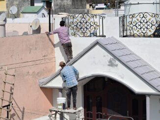 Dva muži malují bílou barvou dům.