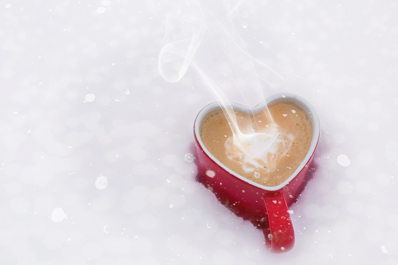 Hrnek s kávou ve tvaru srdce, položený ve sněhu.