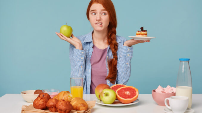 Dívka váhá mezi dietním a sladkým jídlem.