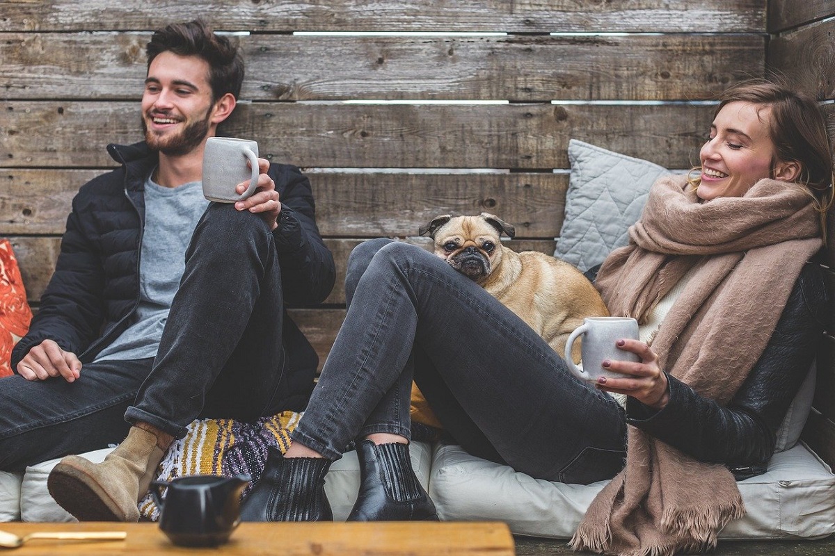 Muž a žena sedí s kávou a psem venku.