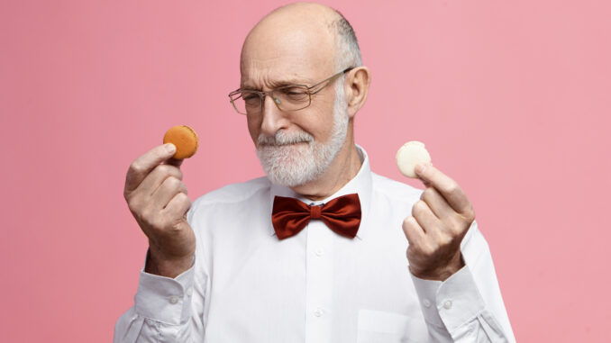 Starší muž drží v každé ruce jednu sušenku.