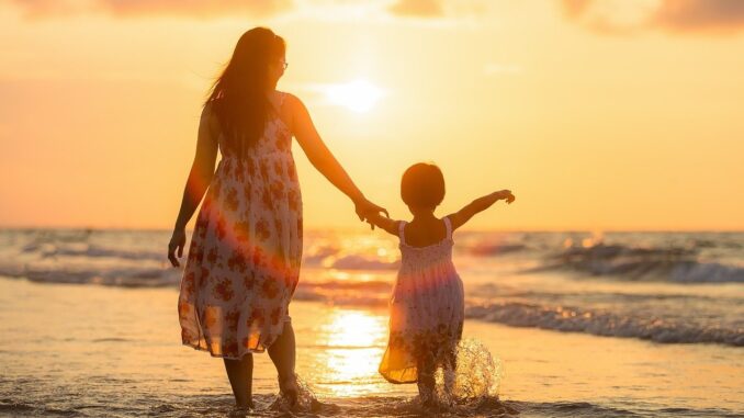 6ena s dítětem se prochází ruku v ruce po pláži