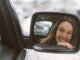 zrcadlo na autě ve kterém je vidět usměvavá žena.