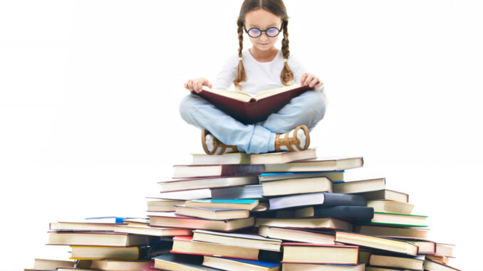 Dívka sedí na hromadě knih.