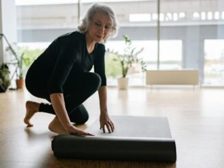 Senior woman setting up yoga mat in bright studio, preparing for exercise.