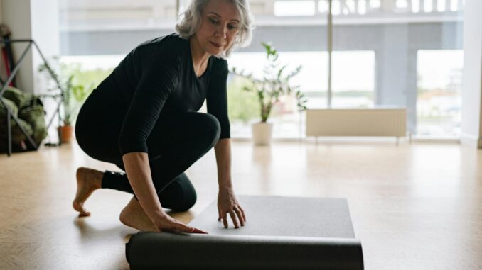 Photo by Yan Krukau Senior woman setting up yoga mat in bright studio, preparing for exercise.