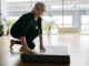 Senior woman setting up yoga mat in bright studio, preparing for exercise.