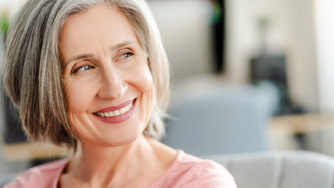 Smiling confident senior woman sitting on comfortable sofa at home. Happy female looking away