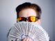 man in black framed sunglasses holding fan of white and gray striped cards