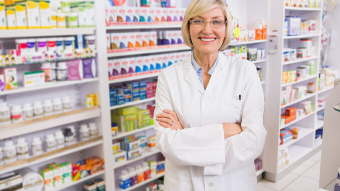 Blonde pharmacist with arms crossed smiling at camera in the pharmacy