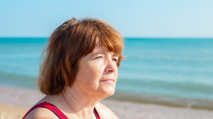 elderly woman looks away at the sea coast. Retirement vacation on a summer day