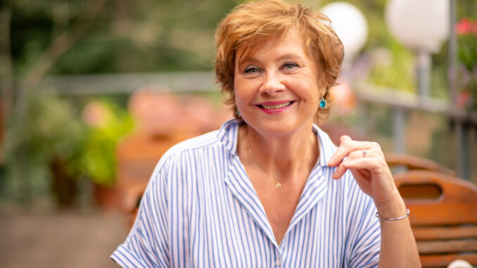 A smiling woman in a casual striped shirt enjoys a sunny afternoon