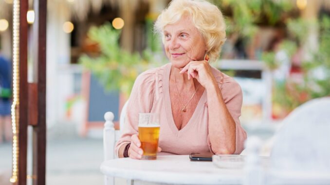 Mature woman sitting at a table in a summer cafe and drinking beer