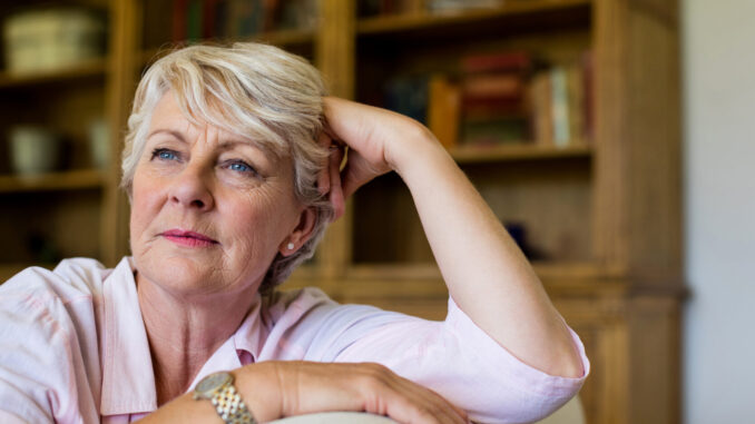 Thoughtful senior woman relaxing on sofa in living room at home