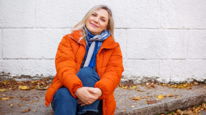 Happy smiling middle aged woman in orange down jacket sitting on
