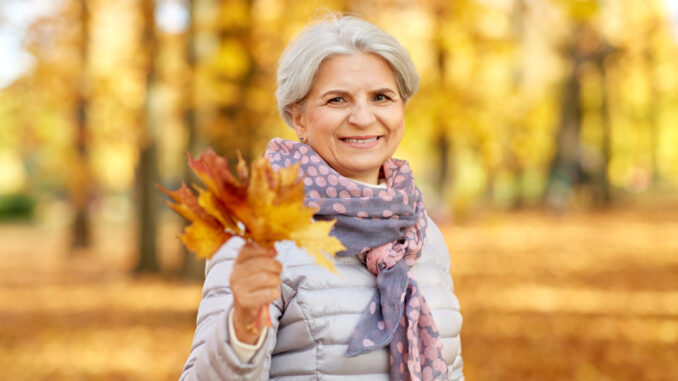 senior woman with maple leaves at autumn park